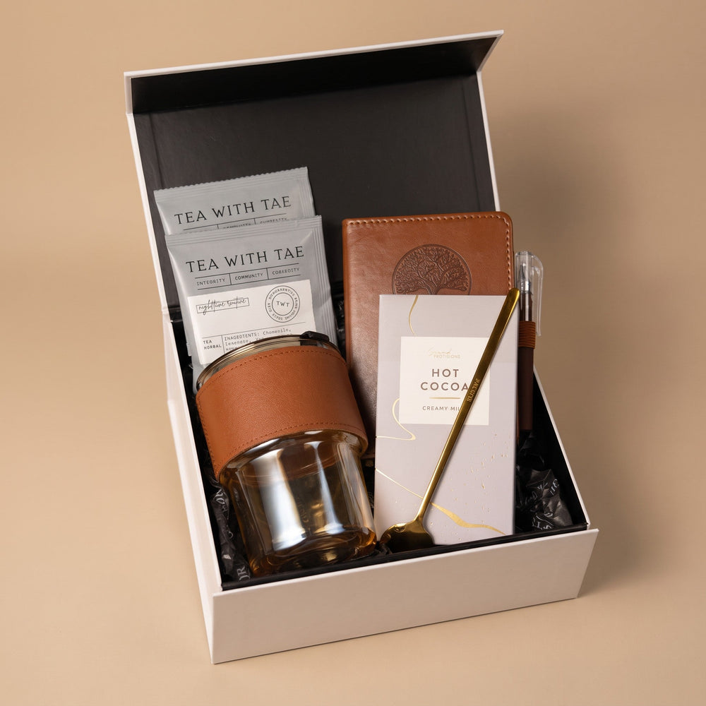 Open keepsake gift box with tea, cocoa, journal, pen and glass cup